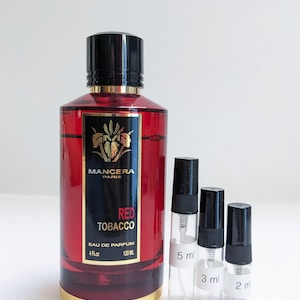 May include: A 120 ml bottle of Mancera Red Tobacco Eau de Parfum with a gold cap and a red label. The bottle is next to three smaller sample bottles labeled 5 ml, 3 ml, and 2 ml.