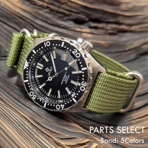 Puede incluir: Un reloj de acero inoxidable con esfera negra y correa de tela verde. El reloj tiene marcas blancas y una ventana de fecha. El texto "LEVEL7" y "WATER RESISTANT 20 BAR AUTOMATIC" son visibles. La correa mide aproximadamente 2 cm de ancho.