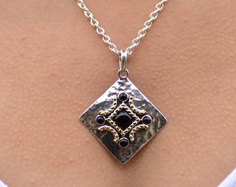 May include: A silver necklace with a square pendant featuring a black gemstone surrounded by gold accents.