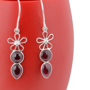 May include: A pair of silver dangle earrings with a flower design and two red gemstones.