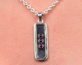 May include: A silver chain necklace with a rectangular pendant featuring three small, round, dark red gemstones.