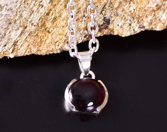 May include: A silver chain necklace with a pendant featuring a dark red oval gemstone.