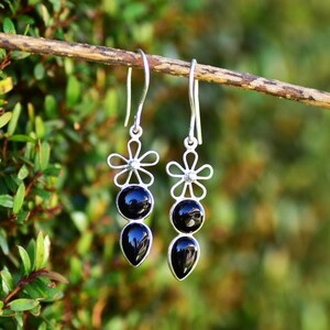 May include: A pair of silver dangle earrings with black gemstone drops and flower accents.
