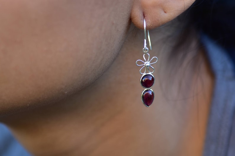 May include: Silver dangle earrings with a flower charm and two red gemstone drops.
