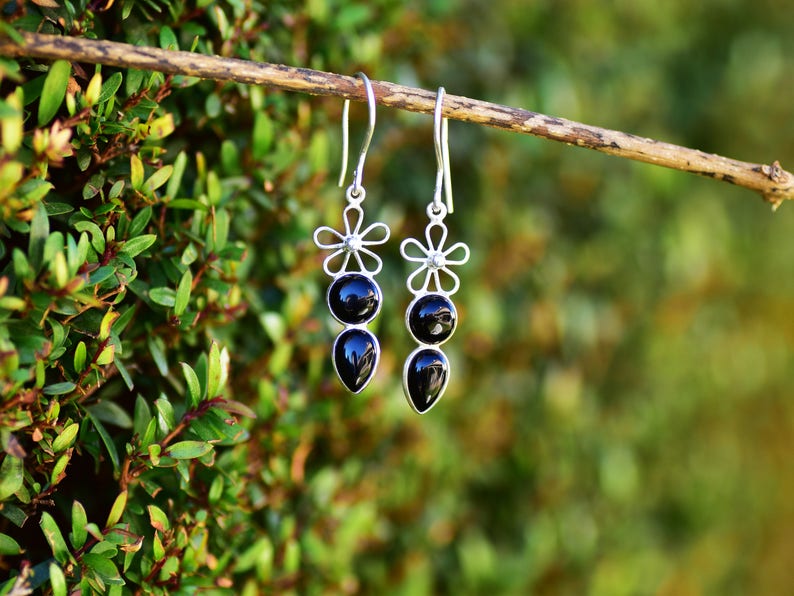 May include: A pair of silver dangle earrings with black gemstone drops and flower accents.