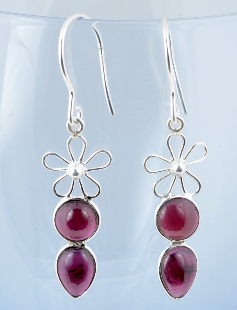 May include: A pair of silver dangle earrings with a flower design and two purple gemstones.