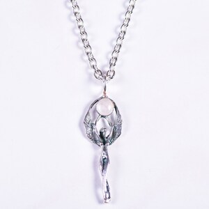 May include: A silver-toned pendant necklace featuring a stylized figure with outstretched wings, holding a round, pale pink stone. The pendant hangs from a silver chain. The design is intricate and detailed, with a focus on the figure's form.