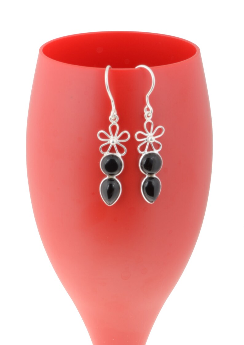 May include: A pair of silver dangle earrings with black gemstone drops and flower accents.