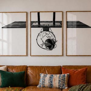 May include: A tan leather sofa with green, orange, and patterned throw pillows, a round wooden coffee table with books, and three framed black and white prints of a basketball hoop hanging on the wall above the sofa with a neon sign reading GOOD VIBES ONLY.