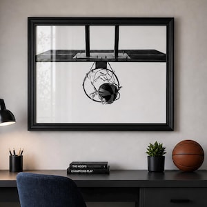 May include: A modern bedroom scene featuring a black desk with a black desk lamp, a basketball, and a framed black and white image of a basketball hoop. A blue chair sits in front of the desk. A bookshelf and bed are in the background.
