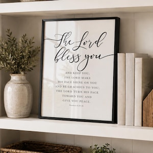 Op de afbeelding: Een ingelijste wandkunstprint met de zwarte tekst The Lord bless you and keep you; the Lord make his face shine on you and be gracious to you; the Lord turn his face toward you and give you peace. Numbers 6:24-26 in script- en schreeflettertype.