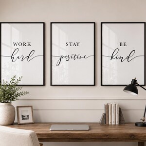 Puede incluir: Tres láminas de pared enmarcadas con fondo blanco y texto en negro. La primera lámina dice WORK hard, la segunda STAY positive y la tercera BE kind. El texto presenta una combinación de fuentes sans-serif en negrita y cursiva.