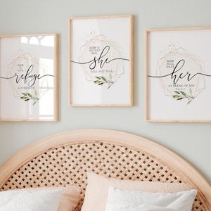 May include: Three framed art prints with inspirational quotes. Each print features elegant calligraphy and geometric designs in gold and black, with botanical accents. The prints are displayed above a bed with white bedding.