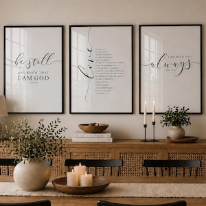 Può includere: Una scena di sala da pranzo con un tavolo in legno, un runner beige e sedie nere. Un mobile in legno con frontale intrecciato espone decorazioni. Tre stampe incorniciate con cornici nere sono appese al muro, ognuna con testo scritto. Una lampada e candele contribuiscono all'atmosfera.
