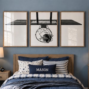 Könnte beinhalten: Ein Schlafzimmer in Blautönen mit einem Bett mit marineblauer Bettwäsche und dekorativen Kissen. Über dem Bett befinden sich drei gerahmte Schwarz-Weiß-Basketball-Drucke. Ein Nachttisch aus Holz mit einer Lampe und ein Bücherregal mit Dekoration vervollständigen den Raum.