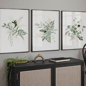 Puede incluir: Tres impresiones bot&aacute;nicas enmarcadas con ilustraciones en acuarela de follaje verde y dorado. Las impresiones se exhiben sobre un mueble negro con frente tejido. Un objeto decorativo y un libro est&aacute;n en el mueble.