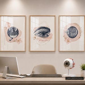 Puede incluir: Tres impresiones enmarcadas en acuarela de ilustraciones relacionadas con el ojo. Cada impresión presenta un tema diferente: un instrumento médico, un ojo y una sección transversal del ojo. Las impresiones están en marcos de madera y se exhiben en una consulta de optometría.