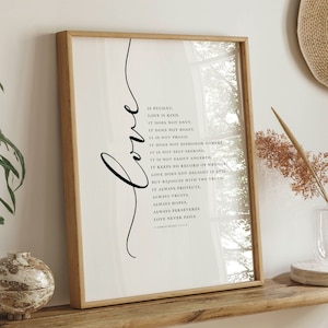 Op de afbeelding: Een ingelijst print met een witte achtergrond en zwarte tekst. De tekst is een citaat over liefde uit 1 Korintiërs 13:4. De print is ingelijst in een licht houten lijst.