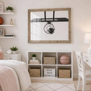 May include: A bedroom scene with a white desk, shelves, and bed. A framed basketball hoop art piece hangs above a white storage unit. A pink basketball and a sign that says "WORK HARD DREAM BIG" are visible.