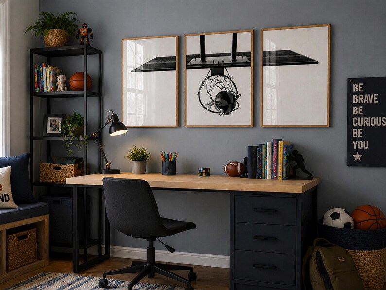 May include: A home office setup featuring a light wood desk with a black three-drawer cabinet, a black office chair, and a black metal shelving unit. Three framed black and white prints of a basketball hoop hang on the gray wall above the desk.