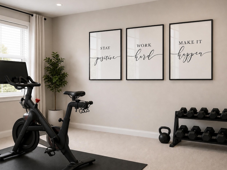 May include: A home gym featuring a black exercise bike, framed motivational art, a dumbbell rack, and a kettlebell. The art pieces read "Stay Positive", "Work Hard", and "Make It Happen" in elegant script.