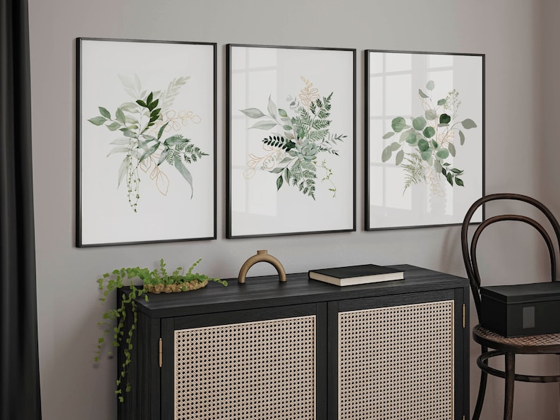Puede incluir: Tres impresiones bot&aacute;nicas enmarcadas con ilustraciones en acuarela de follaje verde y dorado. Las impresiones se exhiben sobre un mueble negro con frente tejido. Un objeto decorativo y un libro est&aacute;n en el mueble.