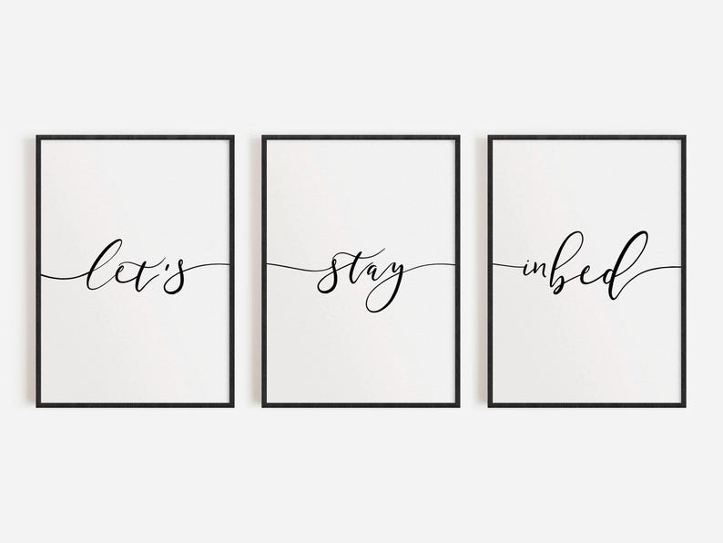 May include: Three black framed prints with white backgrounds and black calligraphy. The prints read "Let's", "stay", and "in bed".