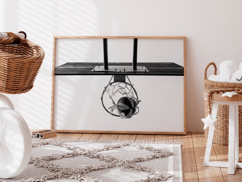 May include: Black and white framed print of a basketball going through a hoop. The image is a close-up shot of the basketball net and ball, with a wooden frame. The print is displayed in a room with a rug and wicker baskets.