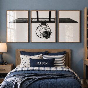 May include: A bedroom featuring a bed with a navy blue quilt, a rectangular pillow with the name MASON embroidered in white, and a set of three framed wall art prints depicting a basketball hoop and ball in a black and white graphic style.