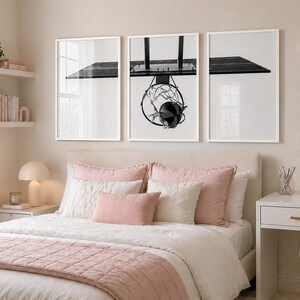 May include: A triptych of framed wall art prints featuring a black and white photograph of a basketball hoop and backboard. The three white frames are arranged horizontally above a bed, displaying a continuous view of the sports equipment.