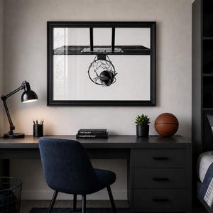 May include: A black desk with a black lamp, a basketball, and a framed black and white image of a basketball hoop. A blue chair sits in front of the desk. A small potted plant and a stack of books are also on the desk.