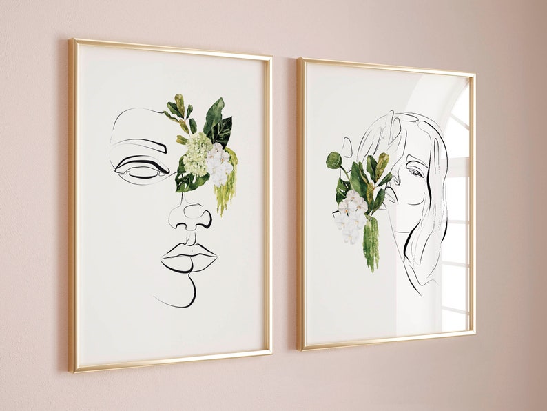 May include: Two framed art prints featuring minimalist line drawings of faces. One print shows a face with an eye, nose, and lips, partially obscured by watercolor flowers. The other print depicts a face with flowing hair and flowers.