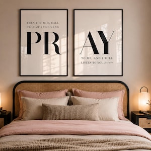 May include: Bedroom decor featuring two framed prints with the words "PRAY" and "PR" in large black letters. A bed with a woven headboard, pink bedding, and decorative pillows is centered below the prints. Two black nightstands with lamps flank the bed.