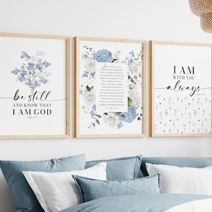 Puede incluir: Tres impresiones artísticas enmarcadas con marcos de madera clara. Las impresiones presentan diseños florales y citas inspiradoras en escritura negra. La paleta de colores incluye blanco, azul y beige. Las impresiones se muestran sobre una cama con ropa de cama azul.