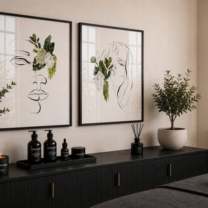 May include: Two framed art prints with black frames, featuring line drawings of faces adorned with floral accents. A black cabinet displays skincare products, a candle, and a diffuser. A small potted plant and a decorative plant are also visible.