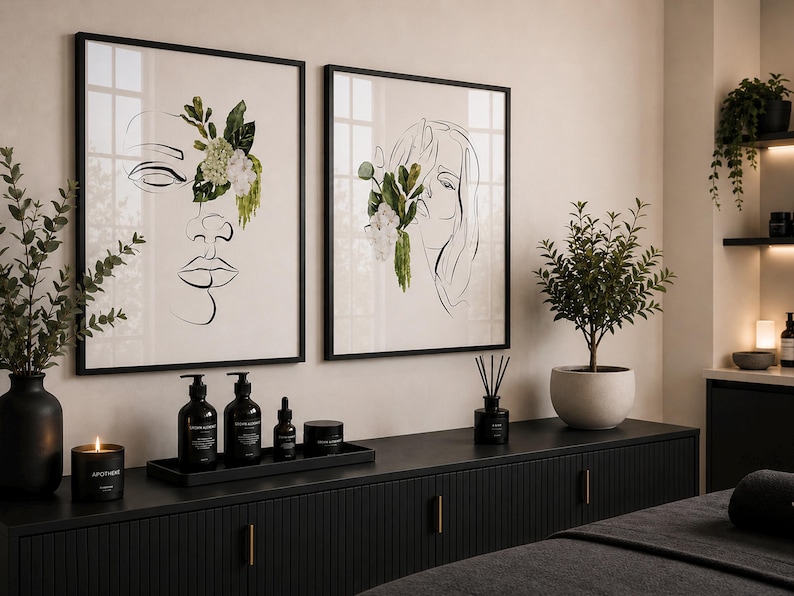 May include: Two framed art prints with black frames, featuring line drawings of faces adorned with floral accents. A black cabinet displays skincare products, a candle, and a diffuser. A small potted plant and a decorative plant are also visible.