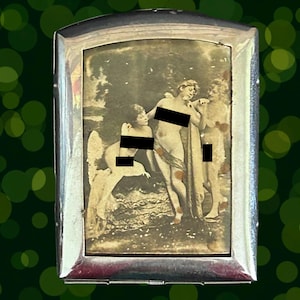 May include: A rectangular silver-toned metal case featuring a sepia-toned vintage illustration of three figures in a landscape setting. The central image is framed by a polished metallic border, and black rectangular bars obscure parts of the figures.