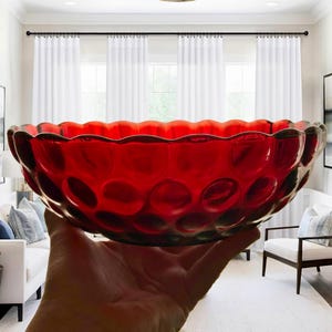 May include: A deep red glass bowl featuring a repeating circular dimpled pattern across its exterior surface and a scalloped, wavy rim. The bowl is translucent, allowing light to pass through the vibrant red material, highlighting the texture.