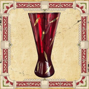 May include: A tall, flared glass vase in a deep ruby red colour, featuring a tapered waist and a wide, open rim. The exterior surface is decorated with scattered, elongated gold leaf-style accents arranged in a vertical, repeating pattern.