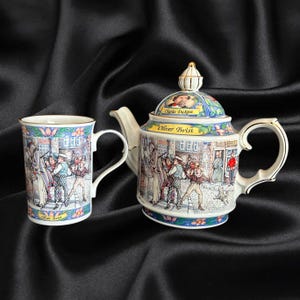 May include: A ceramic teapot and matching mug set featuring colourful illustrations of scenes from Oliver Twist. The teapot lid displays a portrait of Charles Dickens. Both pieces are decorated with floral borders and gold-toned trim accents.