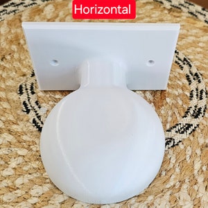 May include: White plastic wall mount with a round, smooth, white sphere attached. The wall mount has two small holes on the top and bottom. The word "Horizontal" is printed in red letters above the wall mount.