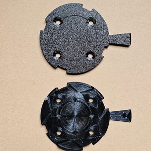 May include: Two black plastic 3D printed parts with a handle and five holes. The top part is smooth and the bottom part has a textured surface.