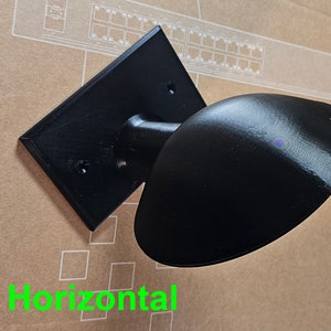 May include: A black wall mount with a round, black, horizontal,  curved,  decorative element. The mount has two screw holes.