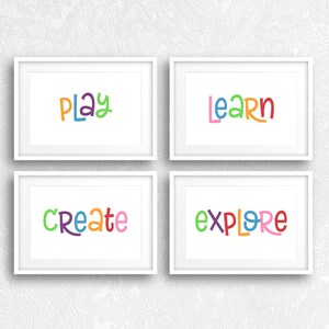 May include: Four framed art prints with the words "PLAY", "LEARN", "CREATE", and "EXPLORE" in colorful, playful lettering. The prints are in white frames and are displayed on a textured white wall.