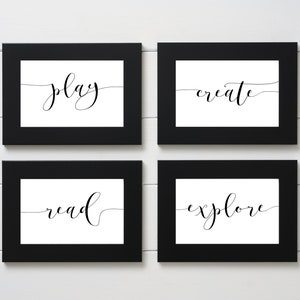 May include: Four framed art prints with the words "play", "create", "read", and "explore" in elegant black script on a white background. The frames are black and the background is a white wood panel.