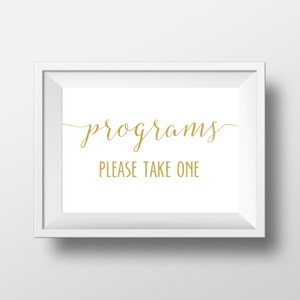 May include: A framed white sign with the words "programs" and "PLEASE TAKE ONE" in gold script. The sign is rectangular and has a white border, suitable for events or informational displays.