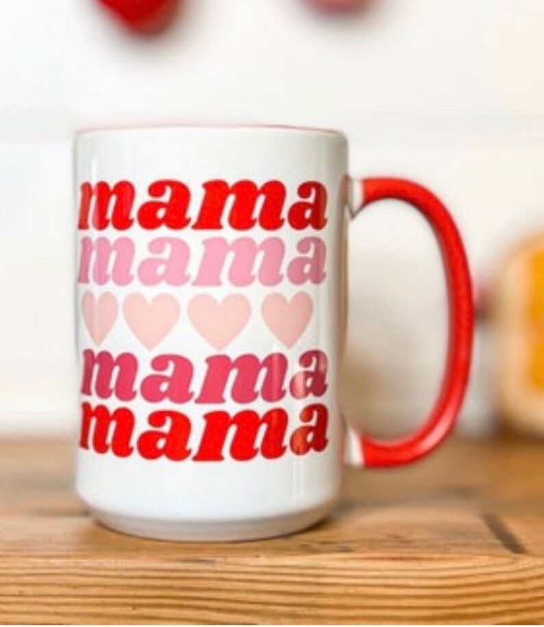Pu&ograve; includere: Una tazza in ceramica bianca con un manico rosso. La tazza ha le parole "mama mama mama mama" stampate su di essa in lettere rosse e rosa con cuori rosa tra ogni parola.