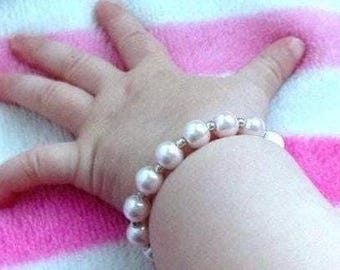May include: A white pearl bracelet with silver beads on a child's wrist.