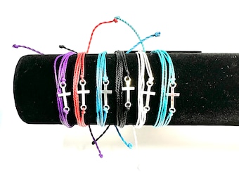 May include: Assortment of colorful friendship bracelets with a silver cross charm. The bracelets are made of braided cord and come in purple, red, blue, black, white, and turquoise.
