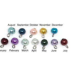 May include: A collection of twelve pearl beads in various colors, each with a silver loop. The months of the year are labeled above and below the beads, from January to December. The beads are in shades of blue, pink, purple, green, and gold.